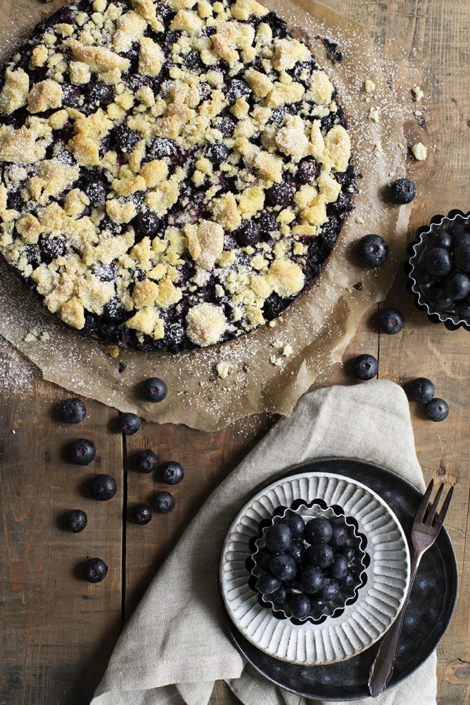 Blaubeerkuchen mit Streuseln, angerichtet mit einer Schale Blaubeeren